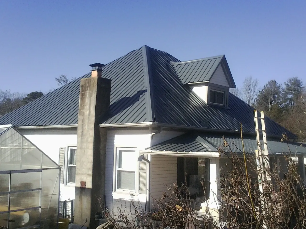 Dark blue standing seam metal roof on a white farmhouse with dormer — Slate & Tile Roof Repair by Roofing Brothers in Wheatcroft