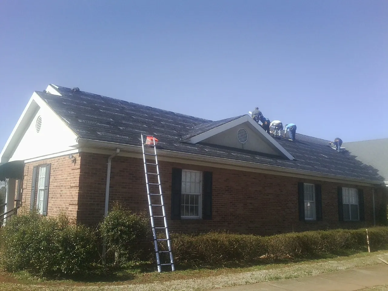 Crew tearing shingles off a brick ranch roof with a ladder set — Metal Roof Repair work by our crew in Wheatcroft