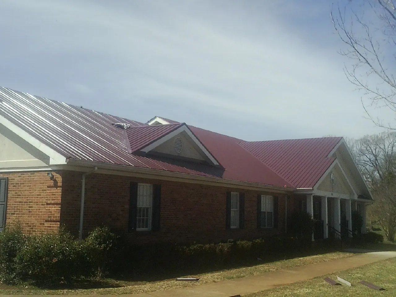 Red metal roof with gabled entries on a long brick building, from a Hail Damage Roof Repair job in Wheatcroft