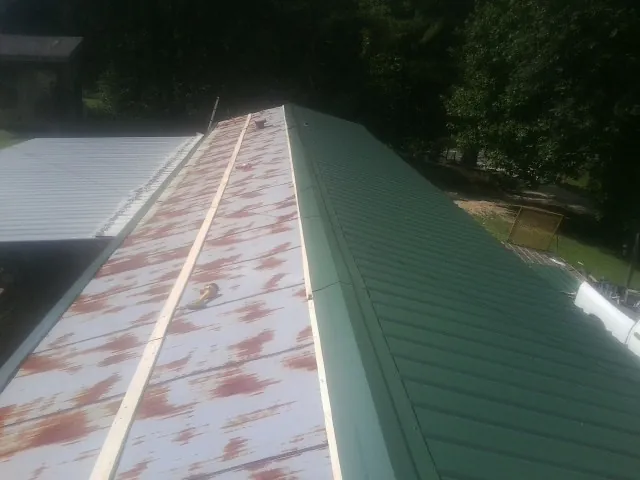Old rusted panels beside newly installed green metal roofing — Wind Damage Roof Repair by Roofing Brothers in Wheatcroft
