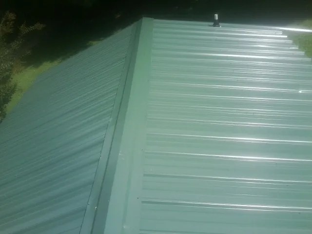 New green metal panels meeting at the ridge of a roof — Flat Roof Repair work by our crew in Wheatcroft