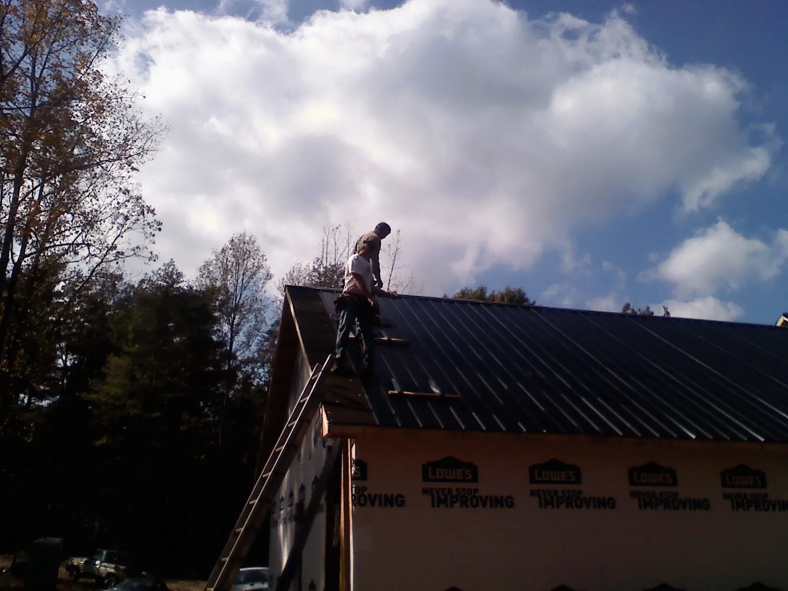 Roofer fastening dark metal panels high against a cloudy sky, from a Roof Inspection job in Wheatcroft