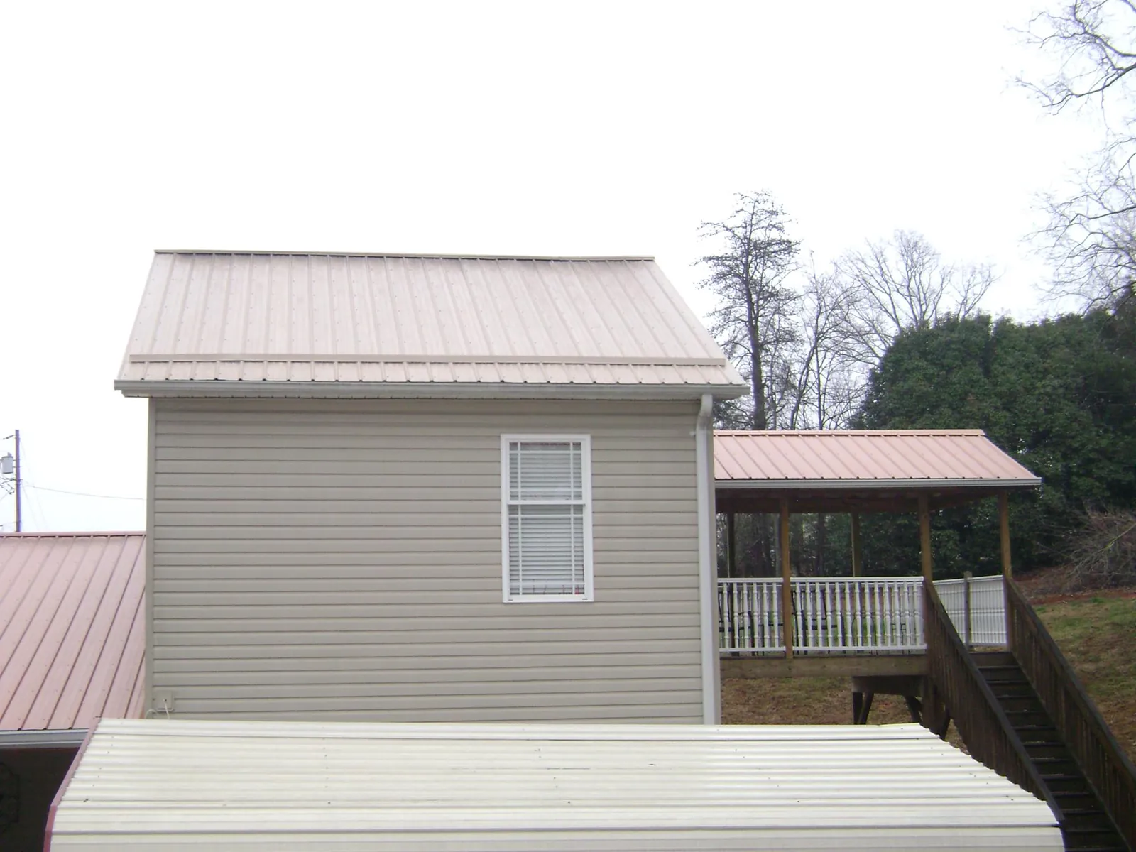 Tan metal roofs on a two story addition and attached porch, from a Roof Replacement job in Wheatcroft
